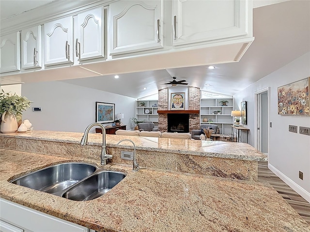 66 Bay Woods Dr, Safety Harbor, FL 34695 - kitchen featuring a sink, ceiling fan, wood finished floors, white cabinetry, and a brick fireplace