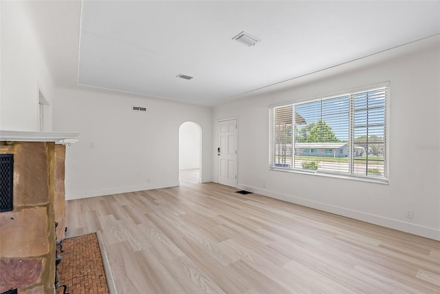 2449 16th St N, Saint Petersburg, FL 33704 - unfurnished living room featuring light wood finished floors, arched walkways, a fireplace, and baseboards