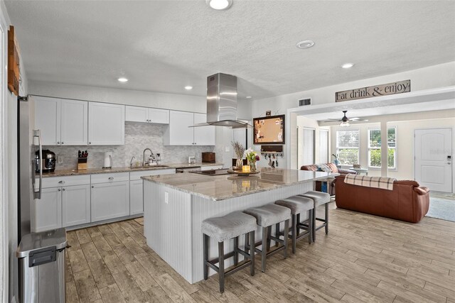 7304 Lakeside Blvd, Tampa, FL 33614 - kitchen with island range hood, a sink, light wood finished floors, open floor plan, and light stone countertops