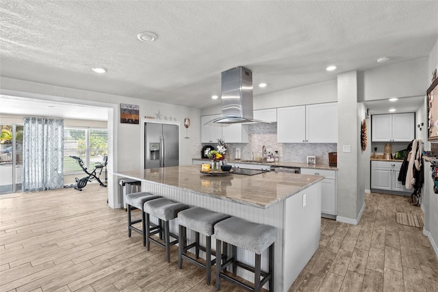 7304 Lakeside Blvd, Tampa, FL 33614 - kitchen with exhaust hood, stainless steel appliances, light wood-style flooring, a kitchen bar, and a textured ceiling