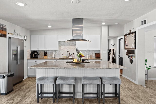 7304 Lakeside Blvd, Tampa, FL 33614 - kitchen with stainless steel fridge, wall chimney range hood, tasteful backsplash, a breakfast bar area, and a textured ceiling