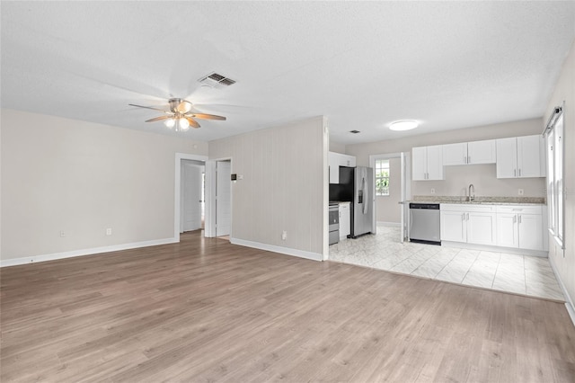 6489 30th St N, Saint Petersburg, FL 33702 - unfurnished living room with light wood-style floors, ceiling fan, baseboards, a textured ceiling, and a sink