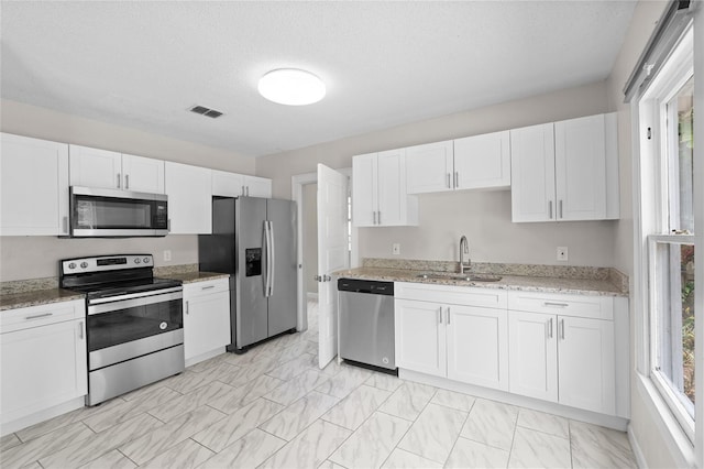 6489 30th St N, Saint Petersburg, FL 33702 - kitchen with stainless steel appliances, a sink, white cabinetry, light stone counters, and light marble finish flooring