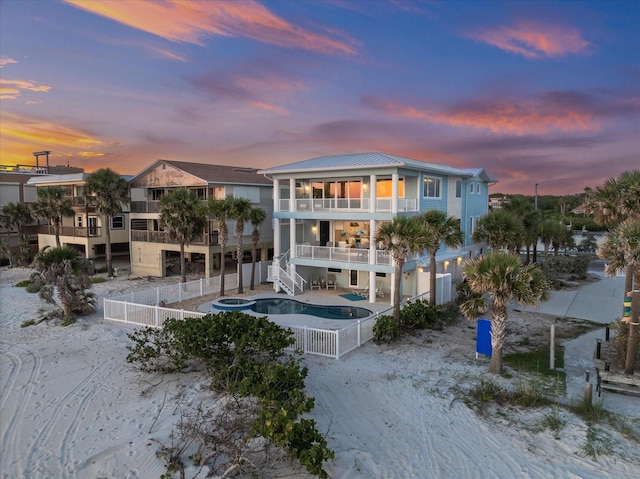 2 Gulf Blvd, Indian Rocks Beach, FL 33785 - back of property at dusk with a balcony, a fenced backyard, an outdoor pool, a patio area, and metal roof
