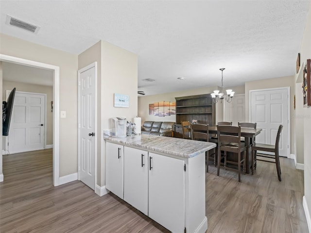 718 Crk 467, Lake Panasoffkee, FL 33538 - kitchen with a peninsula, light wood-style flooring, a chandelier, baseboards, and white cabinetry