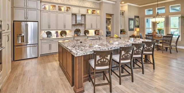 263 Stirling Bridge Dr, Ormond Beach, FL 32174 - kitchen featuring high end refrigerator, crown molding, wall chimney exhaust hood, light stone counters, and light wood-style floors