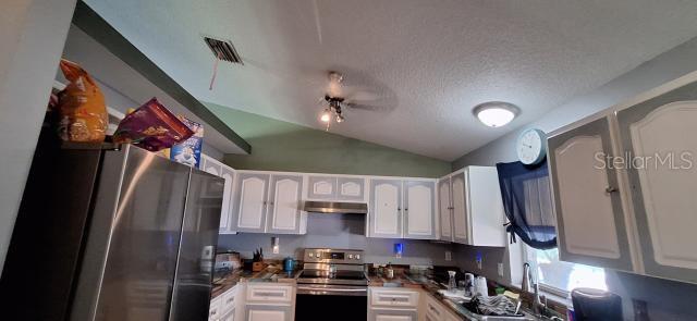 1160 W Geneva Pl, Citrus Springs, FL 34434 - kitchen with appliances with stainless steel finishes, under cabinet range hood, white cabinets, vaulted ceiling, and a textured ceiling