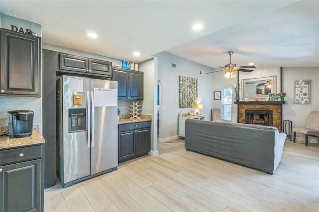 12838 Tallowood Dr, Riverview, FL 33579 - kitchen with stainless steel fridge, a stone fireplace, light wood finished floors, ceiling fan, and light stone counters