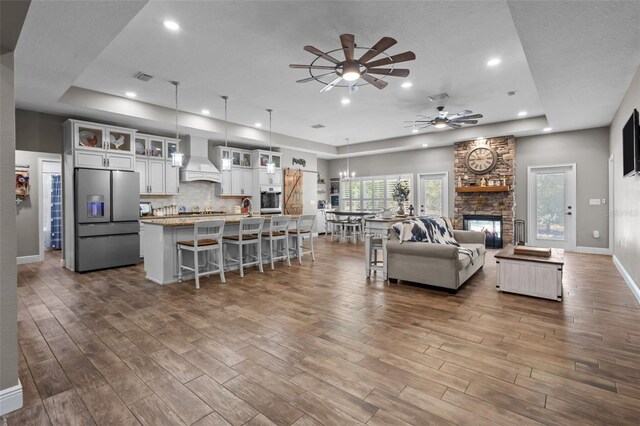 12090 Thames Ave, Weeki Wachee, FL 34614 - living room featuring ceiling fan, a raised ceiling, dark wood-style flooring, a stone fireplace, and recessed lighting