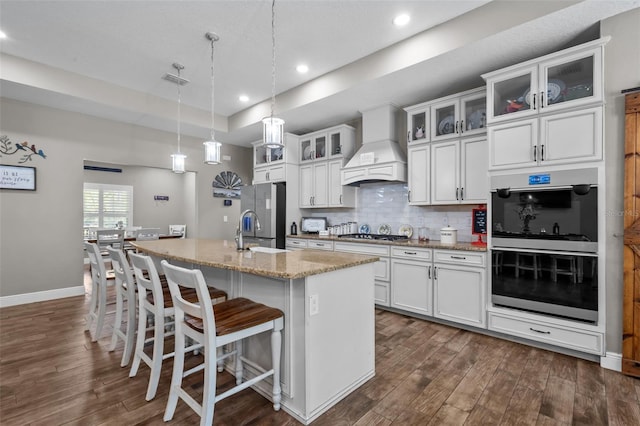 12090 Thames Ave, Weeki Wachee, FL 34614 - kitchen featuring custom range hood, appliances with stainless steel finishes, dark wood-style floors, an island with sink, and tasteful backsplash