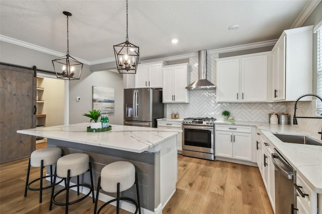 17589 Cruiser Bnd, Land O Lakes, FL 34638 - kitchen featuring appliances with stainless steel finishes, wall chimney exhaust hood, a sink, a kitchen island, and light wood-style flooring