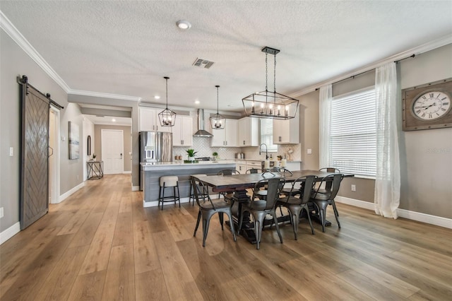 17589 Cruiser Bnd, Land O Lakes, FL 34638 - dining space with crown molding, baseboards, light wood-style flooring, a barn door, and a textured ceiling