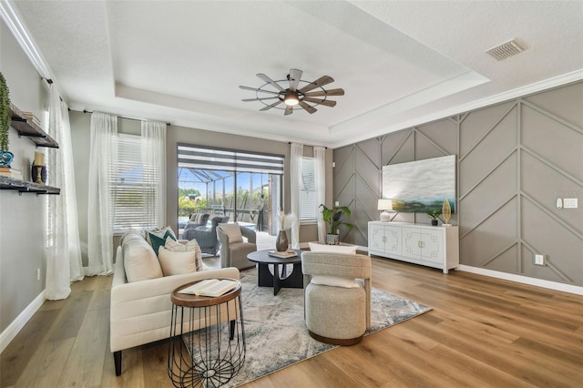 17589 Cruiser Bnd, Land O Lakes, FL 34638 - living area featuring a raised ceiling, wood finished floors, a ceiling fan, baseboards, and a decorative wall