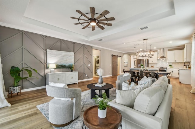 17589 Cruiser Bnd, Land O Lakes, FL 34638 - living room featuring a barn door, stacked washer and clothes dryer, a ceiling fan, a tray ceiling, and light wood finished floors