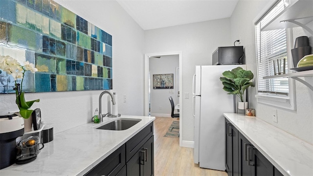 1615 28th Ave N, Saint Petersburg, FL 33713 - kitchen featuring a sink, dark cabinetry, freestanding refrigerator, light wood finished floors, and light stone countertops