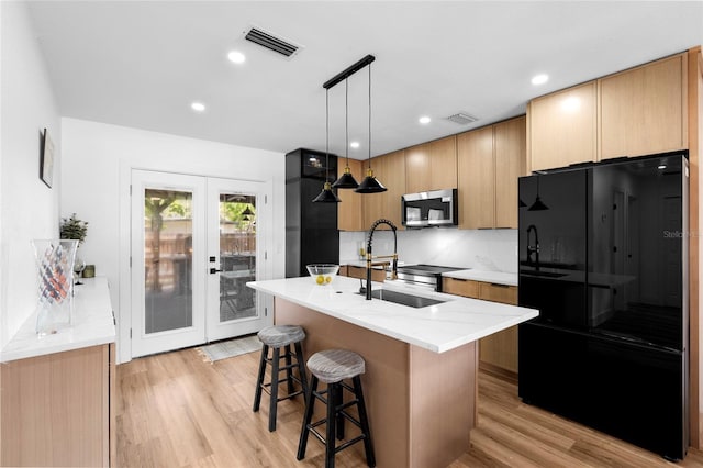 1851 Oklahoma Ave NE, Saint Petersburg, FL 33703 - kitchen with freestanding refrigerator, stainless steel microwave, a sink, light wood-type flooring, and an island with sink
