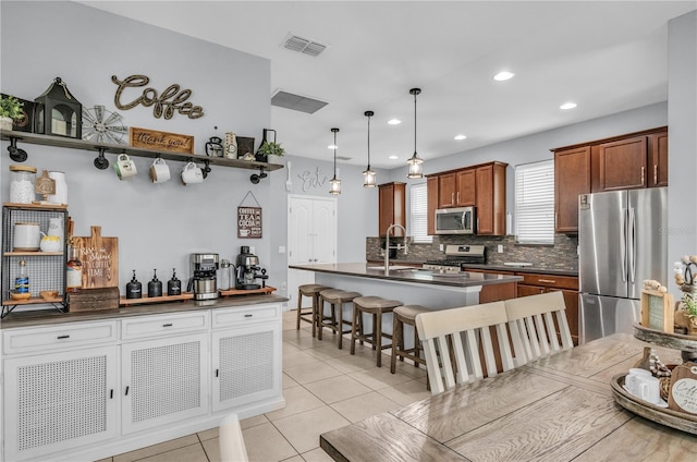 7238 Milestone Dr, Apollo Beach, FL 33572 - kitchen featuring appliances with stainless steel finishes, dark countertops, backsplash, a breakfast bar, and a kitchen island with sink