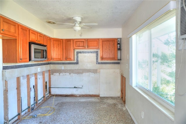14501 N Bayshore Dr, Madeira Beach, FL 33708 - kitchen featuring a ceiling fan, stainless steel microwave, a textured ceiling, brown cabinetry, and baseboards