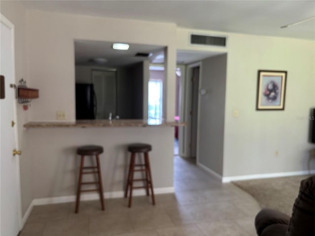 3814 N Lake Dr Unit 65, Tampa, FL 33614 - kitchen featuring refrigerator, a breakfast bar, a peninsula, baseboards, and light tile patterned flooring