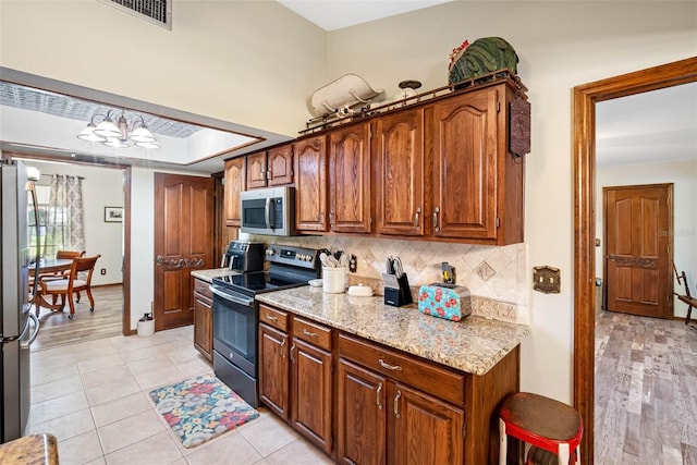 11109 Winn Rd, Riverview, FL 33569 - kitchen featuring appliances with stainless steel finishes, decorative backsplash, light stone counters, baseboards, and brown cabinets