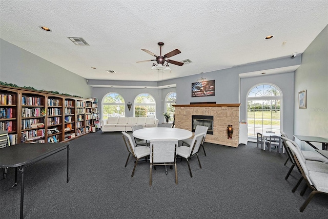 14181 Cornewall Ln, Spring Hill, FL 34609 - dining room featuring dark carpet, a brick fireplace, healthy amount of natural light, a ceiling fan, and a textured ceiling