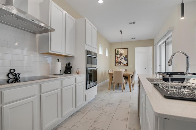 1430 Reunion Blvd, Reunion, FL 34747 - kitchen featuring wall chimney range hood, light marble finish floors, black electric stovetop, double oven, and white cabinets