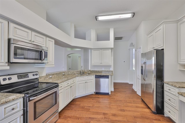 11726 S Stone Ln, Riverview, FL 33569 - kitchen featuring stainless steel appliances, arched walkways, light wood-style flooring, white cabinetry, and light stone countertops