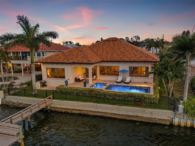 301 Bayview Dr NE, Saint Petersburg, FL 33704 - back of house at dusk featuring a fenced backyard, a water view, a patio, a tiled roof, and stucco siding