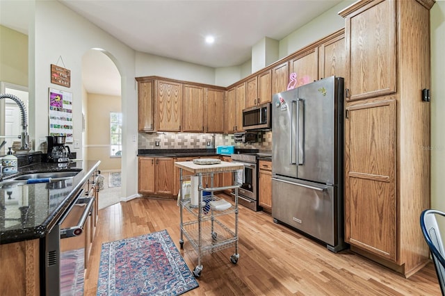 10306 Shalimar Wood Dr, Thonotosassa, FL 33592 - kitchen featuring appliances with stainless steel finishes, a sink, light wood finished floors, arched walkways, and decorative backsplash