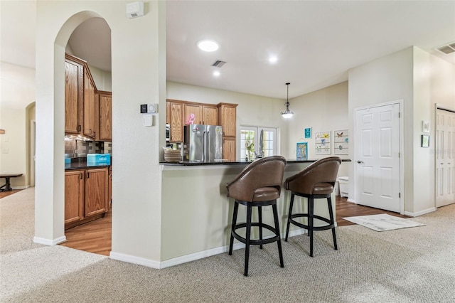 10306 Shalimar Wood Dr, Thonotosassa, FL 33592 - kitchen featuring freestanding refrigerator, carpet floors, arched walkways, a kitchen bar, and brown cabinets