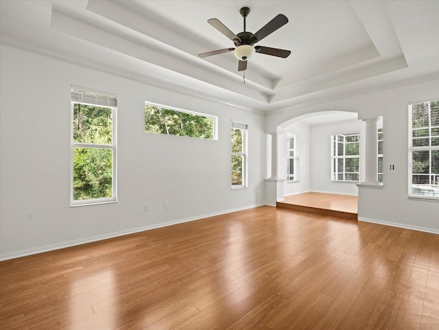 6127 Cezanne Ave, Lutz, FL 33558 - spare room featuring a tray ceiling, ornate columns, arched walkways, ceiling fan, and wood finished floors