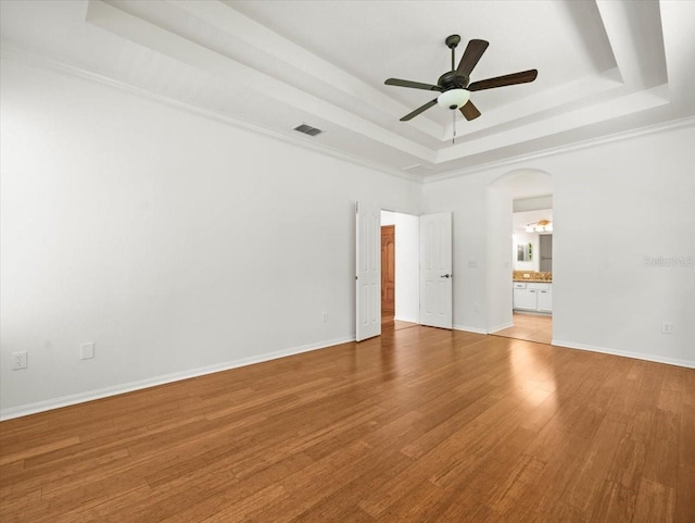 6127 Cezanne Ave, Lutz, FL 33558 - empty room featuring a tray ceiling, ceiling fan, arched walkways, wood finished floors, and baseboards