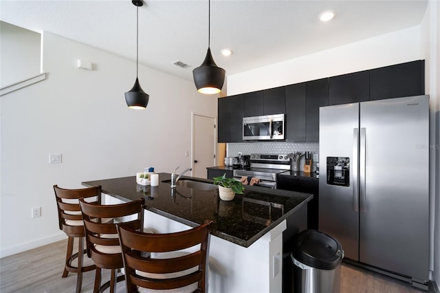 3428 Tranquil Trl, Kissimmee, FL 34747 - kitchen featuring appliances with stainless steel finishes, dark cabinetry, a sink, light wood-type flooring, and a breakfast bar area