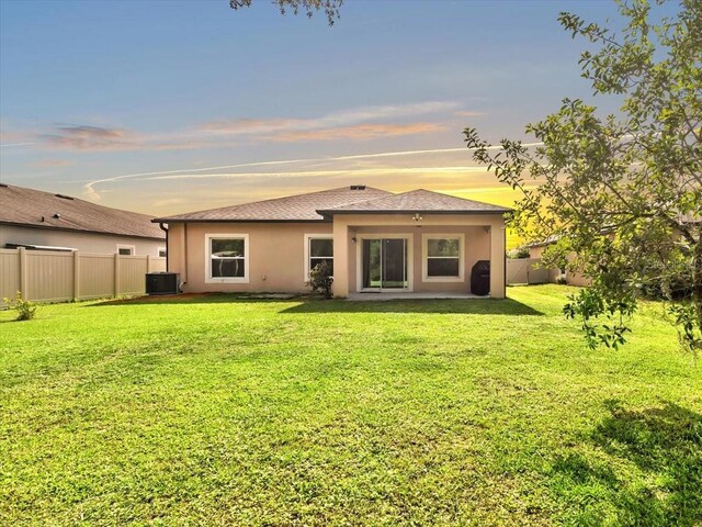 12428 Chaya Ct, Spring Hill, FL 34610 - back of house at dusk with central AC unit, stucco siding, and a shingled roof