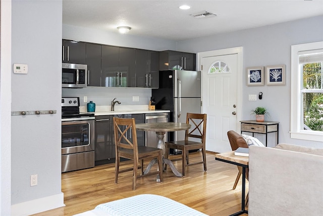 1211 14th St N, Saint Petersburg, FL 33705 - kitchen featuring stainless steel appliances, dark cabinets, light wood-type flooring, light countertops, and a sink
