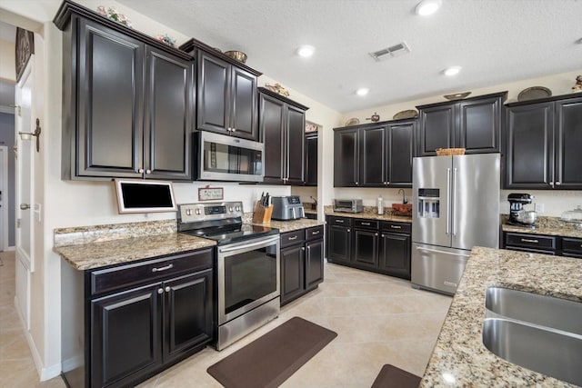 11802 Twilight Darner Pl, Riverview, FL 33569 - kitchen featuring appliances with stainless steel finishes, dark cabinets, light tile patterned floors, light stone countertops, and a textured ceiling