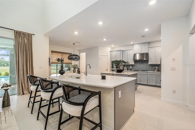 33774 Castaway Loop, Wesley Chapel, FL 33543 - kitchen with under cabinet range hood, a large island, gray cabinetry, gas stovetop, and a breakfast bar