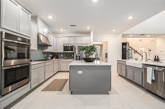 33774 Castaway Loop, Wesley Chapel, FL 33543 - kitchen featuring stainless steel appliances, under cabinet range hood, gray cabinets, a kitchen island, and a sink