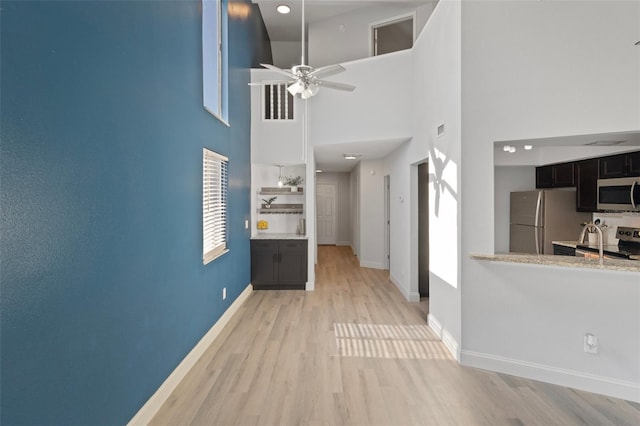 500 New York Ave Unit 23, Dunedin, FL 34698 - unfurnished living room featuring light wood-style floors, a high ceiling, baseboards, ceiling fan, and a sink