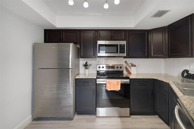 500 New York Ave Unit 23, Dunedin, FL 34698 - kitchen with stainless steel appliances, a raised ceiling, light wood finished floors, decorative backsplash, and light stone counters