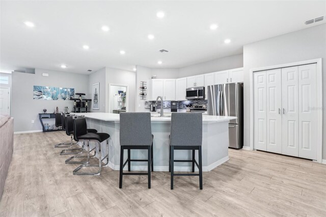 229 St Thomas Dr, Mulberry, FL 33860 - kitchen featuring appliances with stainless steel finishes, white cabinetry, a kitchen island with sink, light countertops, and a breakfast bar