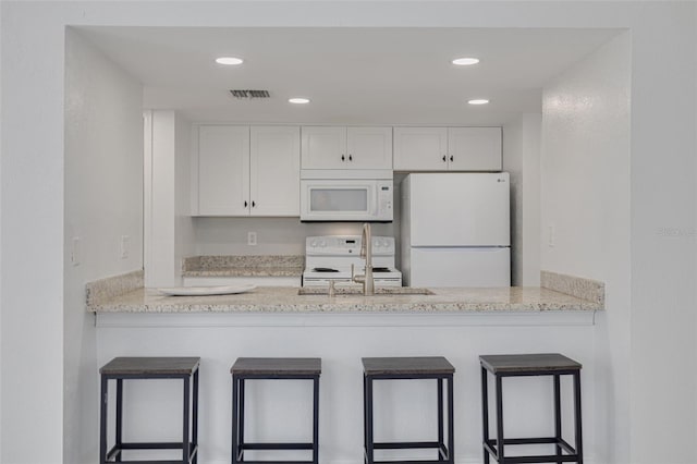 3595 41st Ln S Unit L, Saint Petersburg, FL 33711 - kitchen with white appliances, a peninsula, white cabinets, a breakfast bar area, and recessed lighting