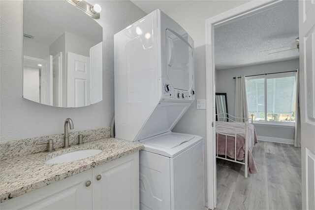 3595 41st Ln S Unit L, Saint Petersburg, FL 33711 - laundry area featuring stacked washer and clothes dryer, light wood-style flooring, and a textured ceiling