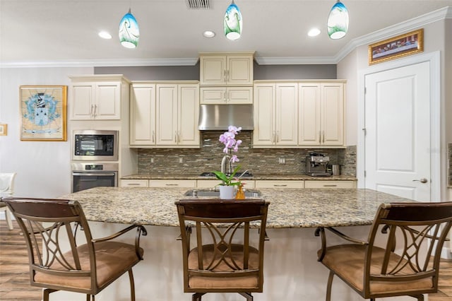 12672 Fontana Loop, Bradenton, FL 34211 - kitchen with under cabinet range hood, stainless steel oven, cream cabinetry, decorative light fixtures, and an island with sink