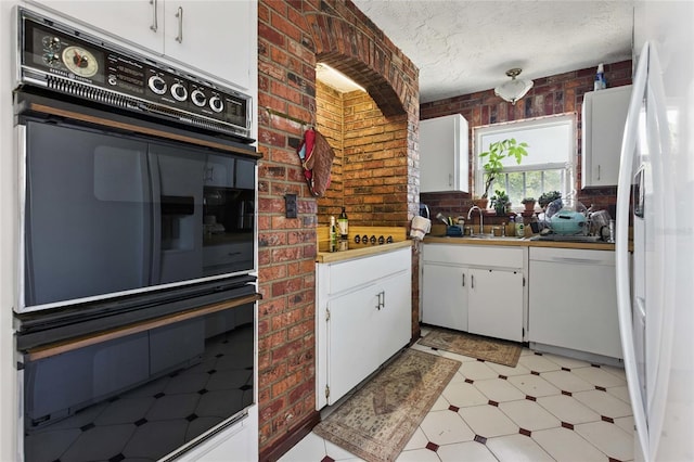 11285 8th St E, Treasure Island, FL 33706 - kitchen with white appliances, light floors, a textured ceiling, white cabinetry, and brick wall
