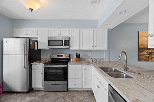 340 Causeway Blvd Unit 104, Dunedin, FL 34698 - kitchen featuring stainless steel appliances, a sink, white cabinets, light stone counters, and light tile patterned flooring