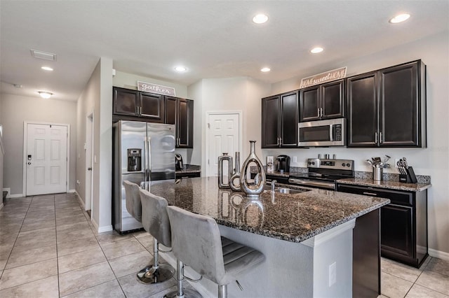 7030 Summer Holly Pl, Riverview, FL 33578 - kitchen with appliances with stainless steel finishes, dark stone countertops, light tile patterned flooring, a center island with sink, and a breakfast bar area