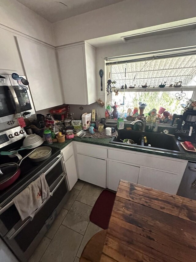 1559 San Roy Dr, Dunedin, FL 34698 - kitchen featuring stainless steel appliances, white cabinetry, a sink, and dark tile patterned floors