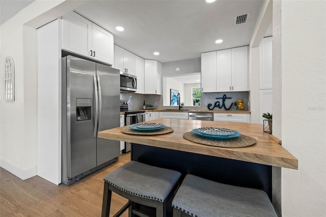 3300 52nd St N, Saint Petersburg, FL 33710 - kitchen with appliances with stainless steel finishes, a breakfast bar, wood counters, light wood-style flooring, and decorative backsplash
