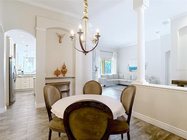 1443 Obear Ct, Wesley Chapel, FL 33543 - dining room featuring crown molding, light wood-type flooring, arched walkways, a chandelier, and decorative columns